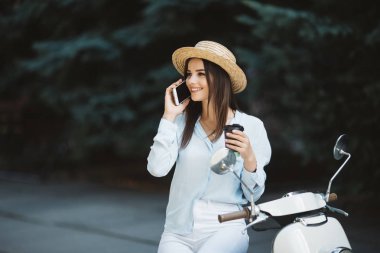 Genç kadın sokakta telefon ve içecek kahve konuşurken motosiklet