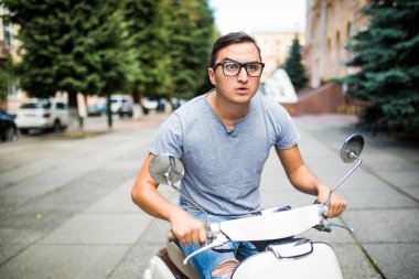 Neşeli genç adam şehirde scooter üzerinde biniyor.