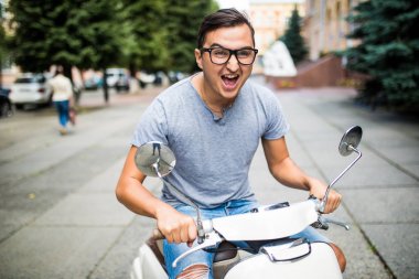 Neşeli genç adam şehirde scooter üzerinde biniyor.