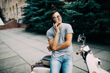 Scooter üzerinde oturan ve cep telefonda konuşurken neşeli genç adam