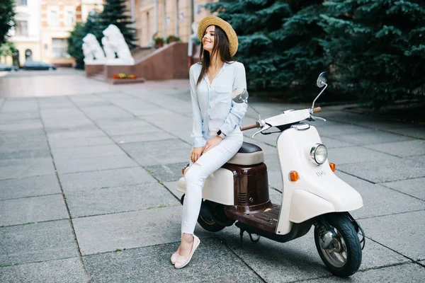 Красота на скутере. Возбужденная молодая и красивая женщина, сидящая возле скутера на улице — стоковое фото
