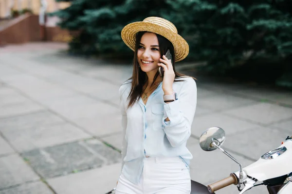 Όμορφη νεαρή γυναίκα ντυμένη casual κάθεται στο σκούτερ και μιλάει στο τηλέφωνο. Κορίτσι, συνεδρίαση για το ποδήλατο και τη χρήση κινητής τηλεφωνίας smartphone — Φωτογραφία Αρχείου