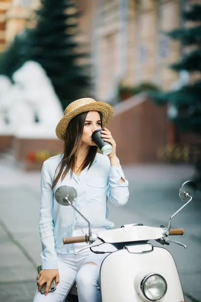 Jovem empresária bebendo um café em uma scooter italiana. Mulher de pé na scooter na rua . — Fotografia de Stock