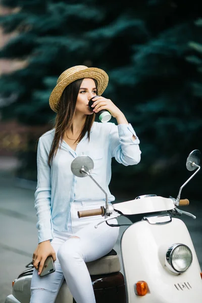 Feliz jovem da moda bebendo café takeaway perto de sua ciclomotor na parte da manhã — Fotografia de Stock