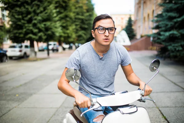 Neşeli genç adam şehirde scooter üzerinde biniyor.