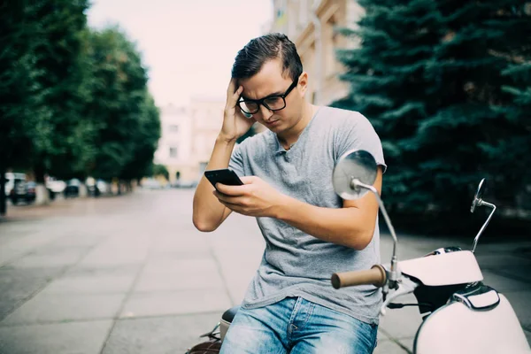 Bir yaz gününde bir scooter üzerinde otururken manifatura cep telefonu üzerinde genç adam