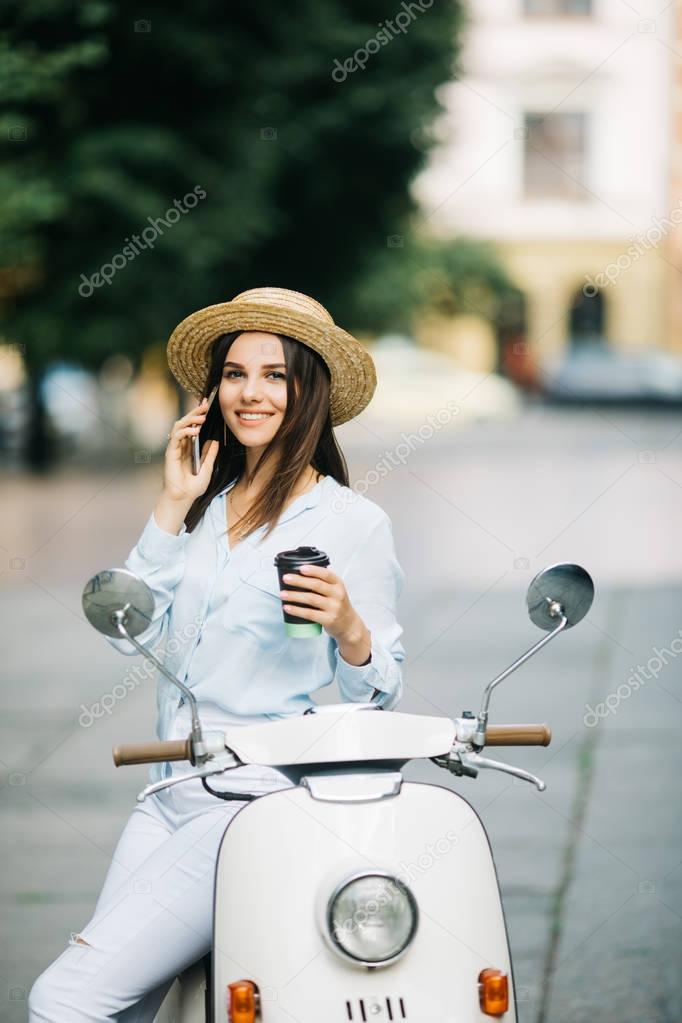 Young woman on motorcycle talking on the phone and drink coffee on the street