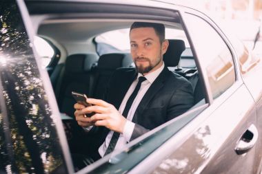 Mobil telefonda konuşurken ve arabanın arka koltuğunda otururken pencere dışında arayan bir işadamı. Erkek iş yürütme bir araba ile seyahat ve telefon görüşmesi.