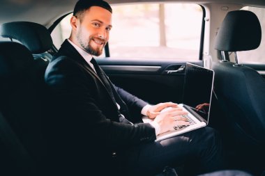 Yakışıklı sakallı işadamı ile dizüstü bilgisayar araba arka koltuk üzerinde çalışma