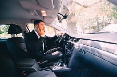 Akıllı telefonda konuşuyor ve ön koltukta otururken gülümseyen yakışıklı genç işadamı