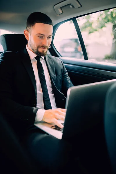 Впевнений молодий бізнесмен працює на ноутбуці і дивиться на камеру, сидячи в машині — стокове фото