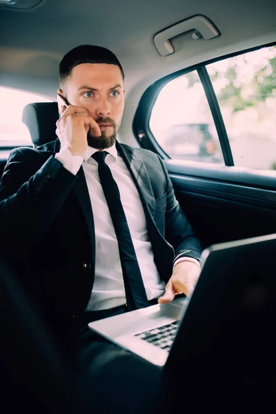 Zeit für eine Entscheidung. selbstbewusster junger Geschäftsmann, der an seinem Laptop arbeitet und im Auto telefoniert — Stockfoto