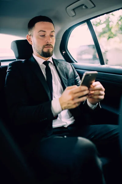 Geschäftsmann im Fond des Autos. SMS auf dem Handy tippen — Stockfoto