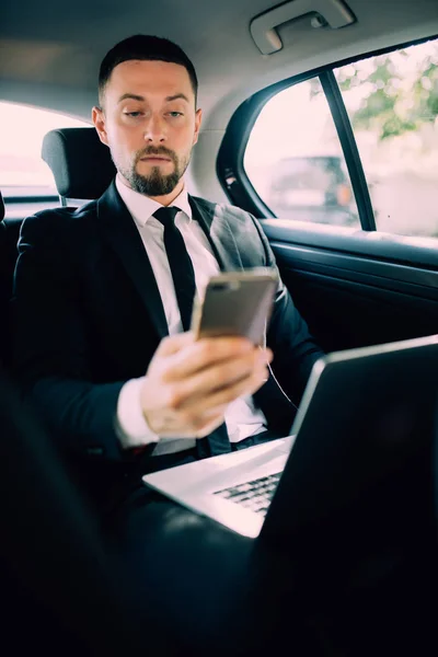 Time to make decision. Confident young businessman working on his laptop and talking on the phone while sitting in the car — Stock Photo, Image