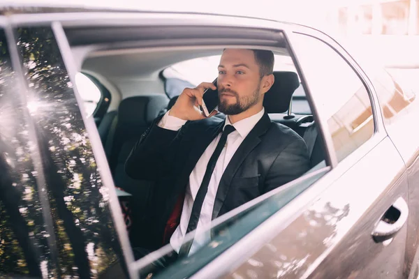 Empresário falando no telefone celular e olhando para fora da janela enquanto sentado no banco de trás do carro. executivo de negócios do sexo masculino viajando de carro e fazendo telefonema . — Fotografia de Stock