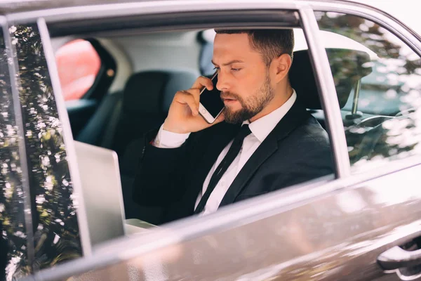 Businessman talking on the mobile phone and looking outside the window while sitting on back seat car — Stock Photo, Image