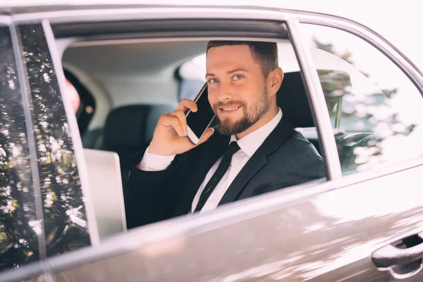 Hombre de negocios serio usando su teléfono en su coche en busca de ventana — Foto de Stock