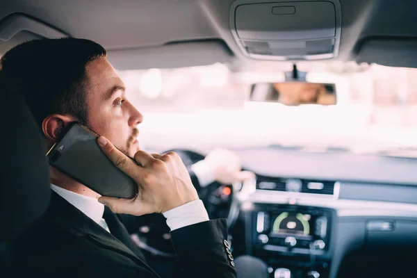Επιχείρηση άνθρωπος βλέπει το κινητό τηλέφωνο κατά την οδήγηση ενός αυτοκινήτου. — Φωτογραφία Αρχείου
