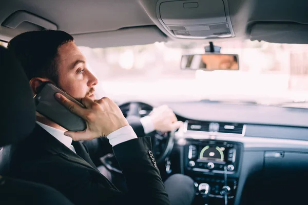 Бизнесмен смотрит на мобильный телефон за рулем автомобиля . — стоковое фото