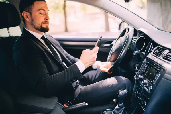 Porträt eines gutaussehenden Geschäftsmannes benutzt Handy im Auto während der Fahrt — Stockfoto