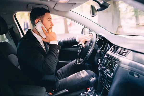 Hombre usando su teléfono mientras conduce el coche. Hombre de negocios conductor hablar teléfono blanco coche — Foto de Stock