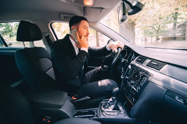 Hombre usando su teléfono mientras conduce el coche. Hombre de negocios conductor hablar teléfono blanco coche — Foto de Stock