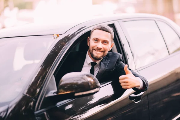 Bonito jovem empresário espancado em um carro com polegares para cima — Fotografia de Stock