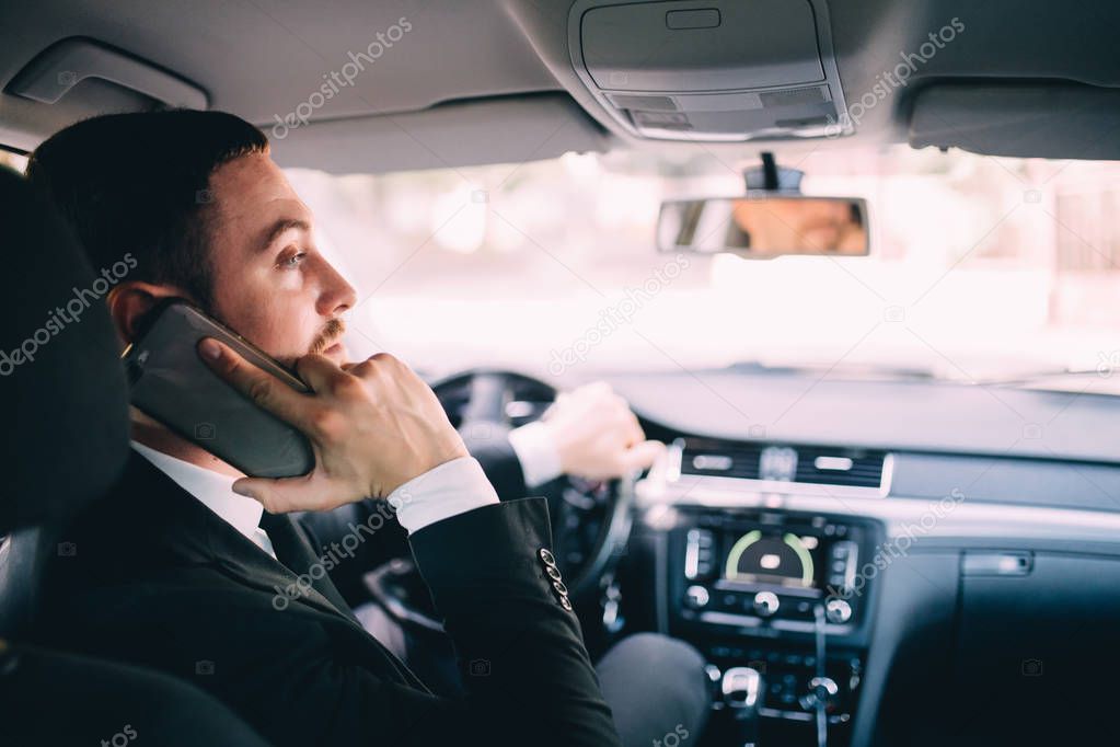 Business Man looking at mobile phone while driving a car.