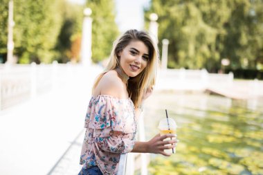 Mesafe içine gülümseyen bir şişe soğuk suyu içme parkta oturan mutlu sarışın kız.