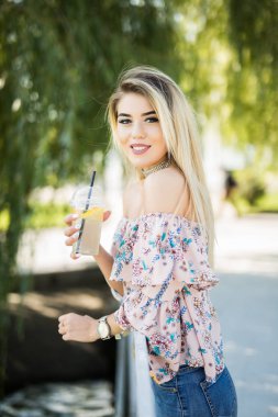 Portakal suyu içme genç mutlu gülümseyen kadın. Güneşli bir gün, açık havada güzel genç kadına yakın çekim.