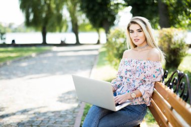 Yaz parkta bankta rahat otururken dizüstü bilgisayar kullanan güzel sarışın kadın