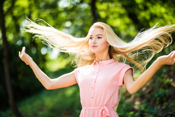 Привлекательная блондинка с кудрявыми волосами в парке, играющая со своими волосами — стоковое фото
