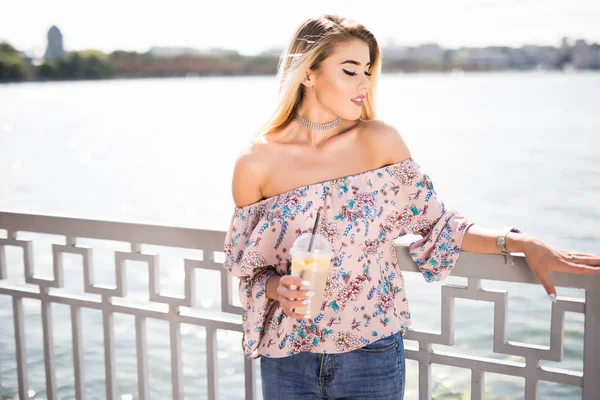 Genç gülümseyen kız şehir nehre çıkabilir oturan ve limonata içmeye. Açık havada yaşam tarzı portre