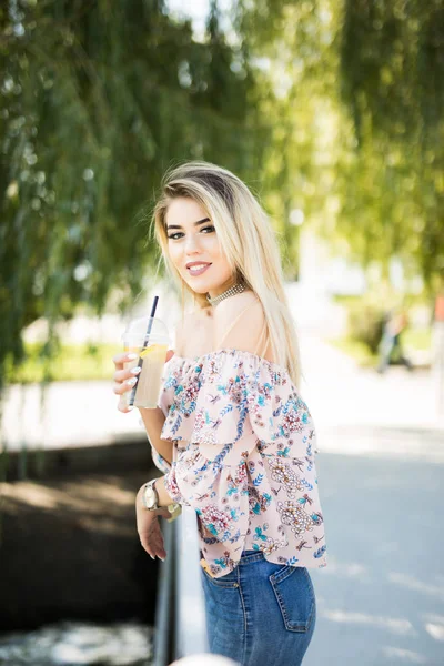 Mesafe içine gülümseyen bir şişe soğuk suyu içme parkta oturan mutlu sarışın kız. — Stok fotoğraf