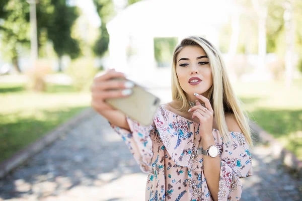 Portret uśmiechniętej młodej dziewczyny robiącej selfie w parku — Zdjęcie stockowe