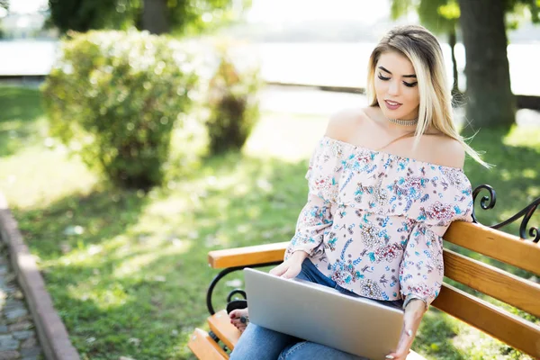 Yaz parkta bankta rahat otururken dizüstü bilgisayar kullanan güzel sarışın kadın