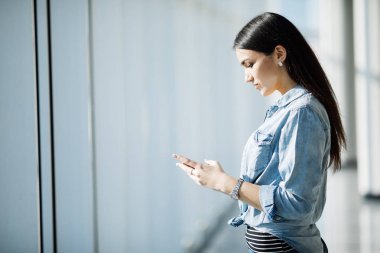 Bir genç kadın metin telefonu panoramik pencerelere karşı portresi