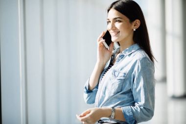 Güzellik kadın konuşmak telefona panoramik pencerelere yakın.
