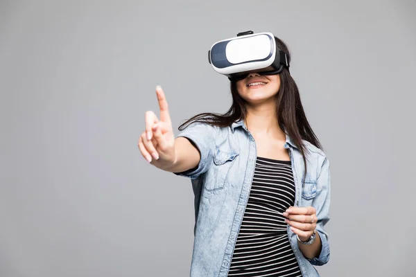 Mujer joven con gafas de realidad virtual y apuntando hacia arriba con el dedo con una expresión seria — Foto de Stock