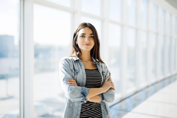 Young beauty woman with crossed hands standing against panoramic windows — Stock Photo, Image