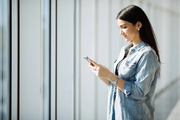 Портрет молодой женщины с текстовым телефоном у панорамных окон — стоковое фото
