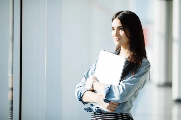 Lavoratrice di successo con computer portatile è in piedi in interni grattacielo contro grande finestra con vista sulla città su sfondo . — Foto Stock