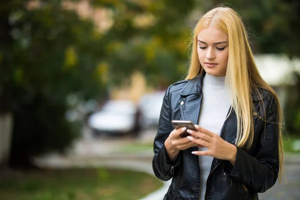 Glad vacker kvinna promenader och skriva eller läsa sms-meddelanden på linjen på en smart telefon medan den på en gata — Stockfoto