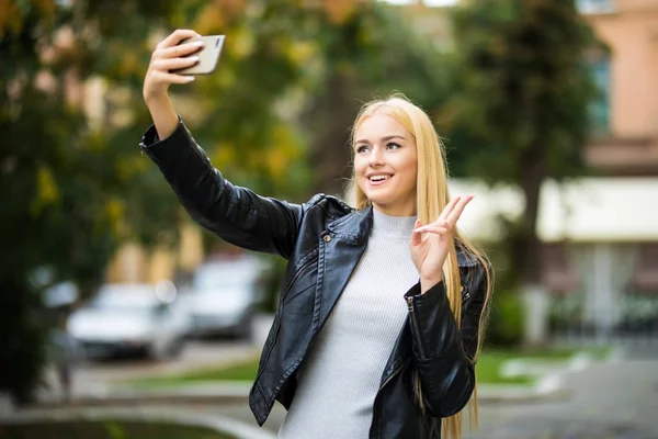 Genç kız, Summer City caddesinde telefonla selfie çekiyor. Kentsel yaşam konsepti.