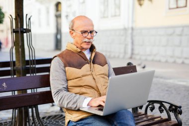 Tezgah şehir sokak güneşli bir günde onun dizüstü bilgisayarda çalışan emekli adam