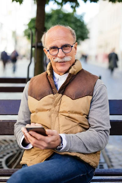 Güzel bir gün zevk. Yazma ve gülümseyen telefon ile tahta bankta oturan neşeli olgun adam.