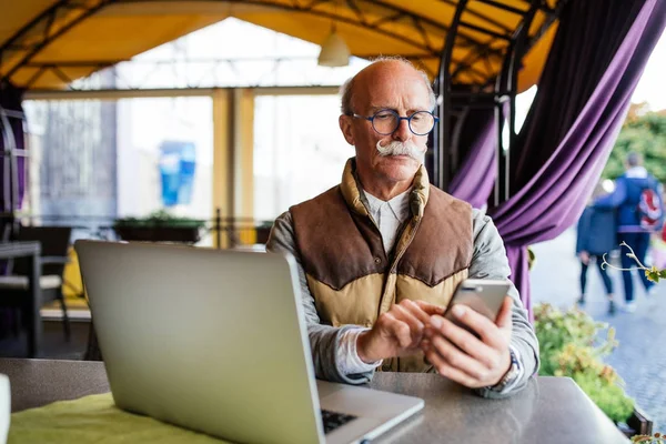Eski üst düzey erkekte ve uygun dizüstü bilgisayar ve smartphone, city café evde oturan ile kravat