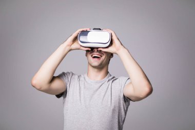 Yakışıklı erkek gri t-shirt, sanal gerçeklik Vr kulaklık gözlükle yaşıyor'portresi kapatın. Gri duvara video oyunları oynarken gözlük, giyen genç adam