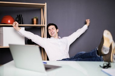 Yapılan işten memnun. Ofisinde çalışırken dizüstü bilgisayarda çalışan mutlu genç adam.