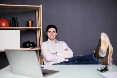 Yapılan işten memnun. Ofisinde çalışırken dizüstü bilgisayarda çalışan mutlu genç adam.